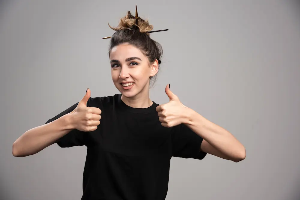 young-woman-with-messy-bun-giving-thumbs-up-gray-wall